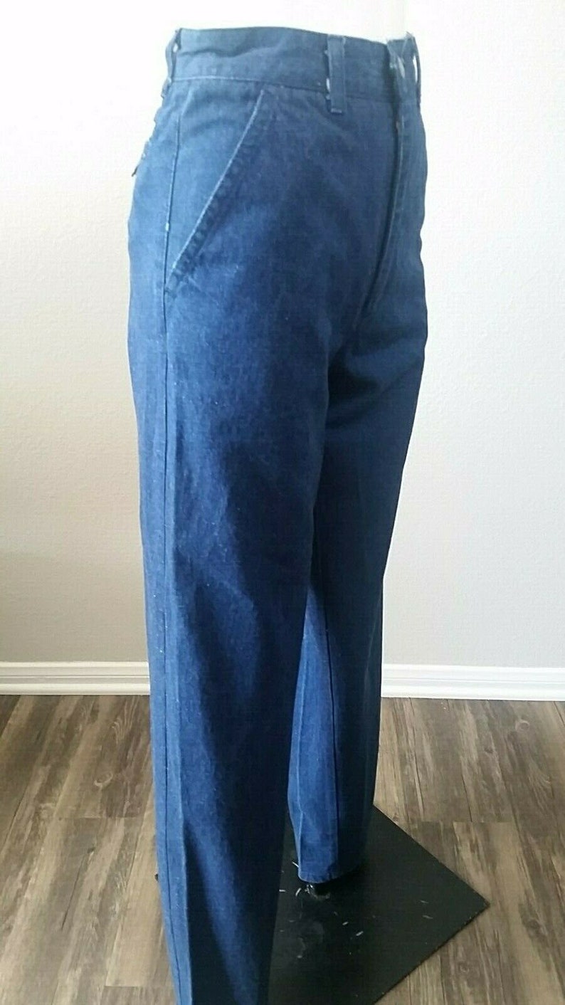 Pu&ograve; includere: Un paio di jeans in denim blu scuro con gamba dritta. I jeans hanno un design classico a cinque tasche e una chiusura a zip.