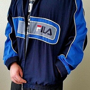 Puede incluir: Una chaqueta azul marino con detalles en azul y gris. La chaqueta tiene cierre de cremallera y un logotipo de Fila en la parte delantera.