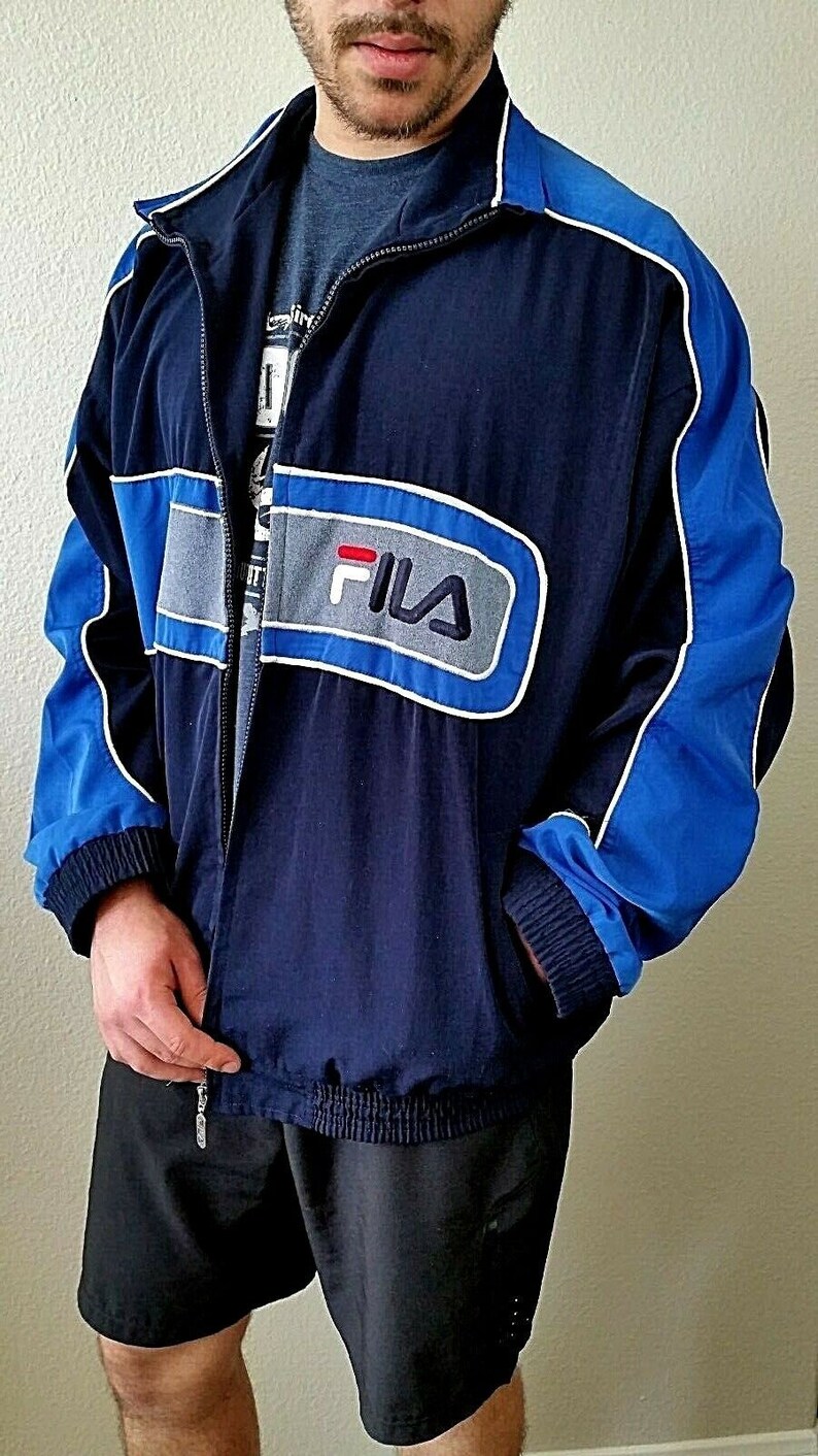 Puede incluir: Una chaqueta azul marino con detalles en azul y gris. La chaqueta tiene cierre de cremallera y un logotipo de Fila en la parte delantera.