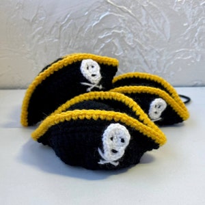 May include: Four crocheted pirate hats with black fabric and yellow trim. Each hat features a white skull and crossbones design.
