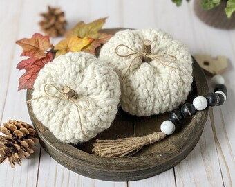 May include: Two white crocheted pumpkins on a wooden tray with a black and white beaded garland and a brown tassel. The pumpkins have a rustic wooden stem and are tied with twine.