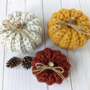 May include: Three crocheted pumpkins in white, yellow, and red. The pumpkins are decorated with twine bows and wooden stems.