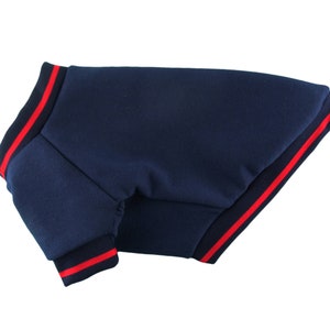 May include: A navy blue dog sweater with red and black trim. The sweater has a ribbed collar and cuffs.