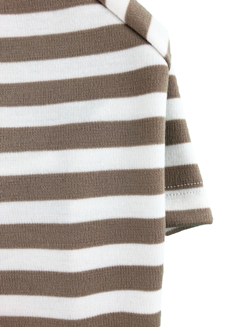 May include: Close-up of a brown and white striped fabric. The fabric is folded over on itself, showing the stitching on the edge.