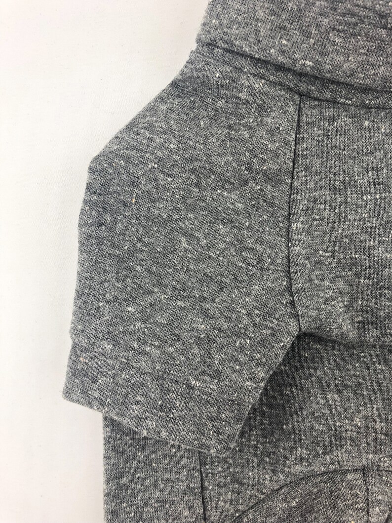May include: A close-up of the gray heather fabric of a short-sleeved shirt. The fabric has a textured, slightly speckled appearance.