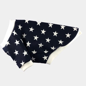 Puede incluir: Un suéter para perro azul marino con un patrón de estrellas blancas. El suéter tiene un ribete blanco alrededor del cuello y las mangas.