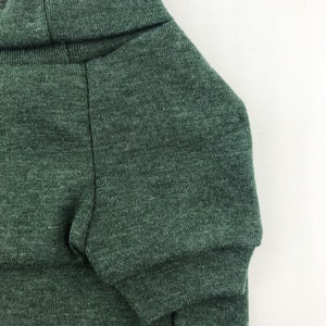 May include: A dark green turtleneck sweater for a pet. The sweater is made of a soft, knitted fabric.