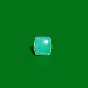 Puede incluir: Un anillo con una piedra grande, cuadrada, lisa y de color turquesa claro, engastada en un sencillo bisel de metal plateado. La piedra muestra variaciones naturales en el color y la textura, con una superficie pulida que refleja la luz.