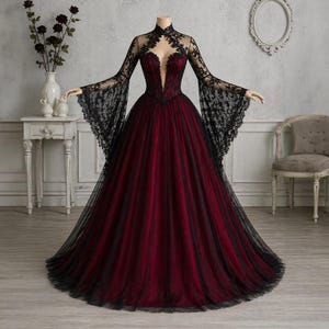 Peut inclure: Une robe de soirée avec un corsage rouge foncé et une jupe en tulle noir. La robe présente de longues manches évasées en dentelle noire et un col montant orné de dentelle. La robe est présentée sur un mannequin sans tête.