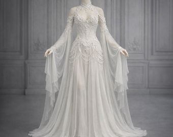 May include: A white wedding dress on a mannequin. The dress features a high neckline, long, flowing sleeves, and intricate lace detailing on the bodice. The skirt flows to the floor. The dress is displayed against a neutral background.
