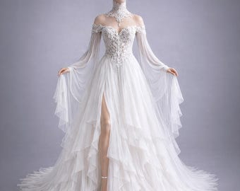 May include: A white wedding dress with a high neckline and off-the-shoulder sleeves. The bodice is embellished with intricate lace and beading. The skirt features multiple layers of flowing fabric, and a high slit reveals the leg. The dress is displayed on a mannequin.