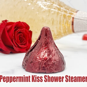 May include: A red peppermint kiss chocolate candy wrapped in foil, a red rose, and a bottle of champagne.  The text "Peppermint Kiss Shower Steamer" is at the bottom of the image.