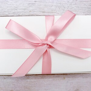 May include: A white gift box with a pink satin ribbon tied in a bow.