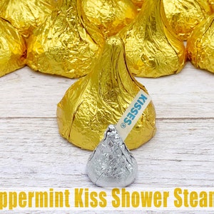 May include: A single silver peppermint kiss shower steamer surrounded by a ring of gold foil wrapped chocolate kisses. The gold foil kisses have the word "KISSES" printed on them.