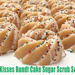 May include: A close-up of several small bundt cake shaped sugar scrub soaps. The soaps are decorated with white, red, and green sprinkles and a white swirl on top. The soaps are arranged on a white surface. The text "Elf Kisses Bundt Cake Sugar Scrub Soap" is written in green letters at the bottom of the image.