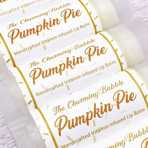 May include: Four white tubes of lip balm with gold labels. The labels have a white background with gold polka dots and the text "The Charming Bubble Pumpkin Pie Handcrafted Vitamin Infused Lip Balm".