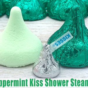 May include: A green peppermint-scented shower steamer shaped like a Hershey's Kiss. The steamer is next to a silver foil-wrapped Hershey's Kiss.