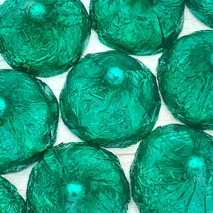 May include: A group of green foil-wrapped chocolate candies. The candies are arranged in a close-up view, showing the texture of the foil.