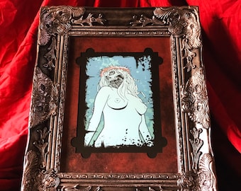 May include: A silver ornate picture frame with a red mat and a black and white illustration of a woman with a skull face and a crown of thorns. The illustration is set against a blue and white background.