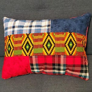 May include: A rectangular throw pillow featuring a patchwork design. The top section has blue and white plaid and solid blue fabric. The middle band displays a vibrant geometric pattern in red, yellow, green, and black. The bottom has red and plaid fabric.