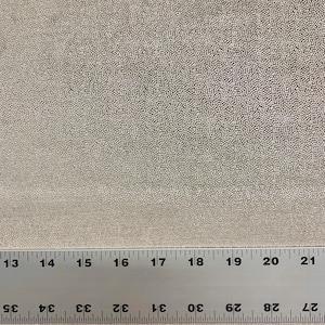 May include: A close-up of a beige fabric with a textured surface. A ruler is placed on the fabric, showing measurements in inches.
