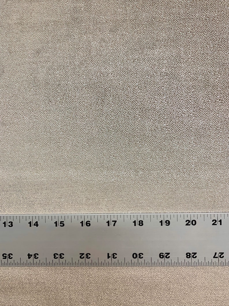 May include: A close-up of a beige fabric with a textured surface. A ruler is placed on the fabric, showing measurements in inches.