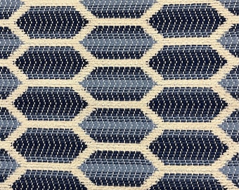 May include: Close-up of a woven textile with a repeating geometric pattern. The design features dark navy blue, light blue, and off-white hexagonal shapes. The texture appears to be made of interwoven threads, creating a textured surface.