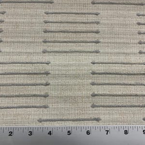 May include: Close-up of a beige fabric with a textured pattern. The pattern consists of horizontal gray lines with small, raised dots. A metal ruler with inch markings is at the bottom of the image.