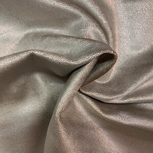 May include: Close-up of a soft, textured fabric with a subtle shimmer. The fabric is a light beige color and has a slightly iridescent sheen.