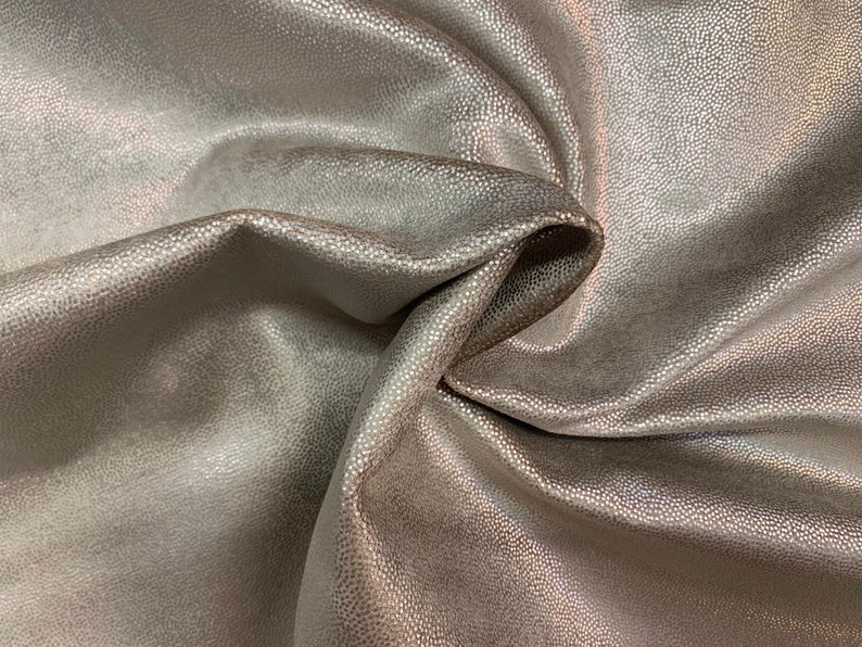 May include: Close-up of a soft, textured fabric with a subtle shimmer. The fabric is a light beige color and has a slightly iridescent sheen.