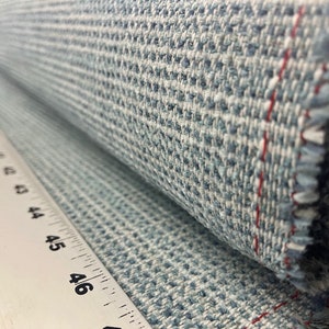 May include: Close-up of a blue and white patterned fabric with a red thread running along the edge. The fabric is rolled up and a ruler is visible in the background.