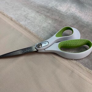 May include: A pair of silver and green scissors with a white handle. The scissors have the words "CARBO TITANIUM" printed on the blade.