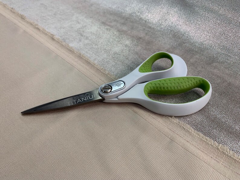 May include: A pair of silver and green scissors with a white handle. The scissors have the words "CARBO TITANIUM" printed on the blade.