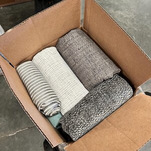 May include: A cardboard box filled with rolls of fabric in various colours and patterns, including grey, white, and blue.