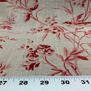 May include: Close-up of a beige fabric with a red floral pattern. The fabric features a repeating design of stylised birds and flowers. A ruler is placed at the bottom of the image, showing measurements in inches.