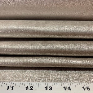 May include: Close-up of a silver faux leather fabric with a textured, pebbled surface. A ruler is visible at the bottom of the image with markings from 10 to 16 inches.