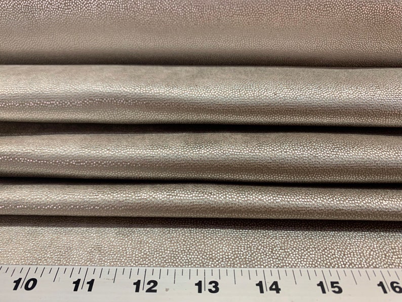 May include: Close-up of a silver faux leather fabric with a textured, pebbled surface. A ruler is visible at the bottom of the image with markings from 10 to 16 inches.