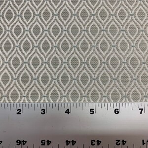 May include: A close-up of a white fabric with a repeating pattern of gray and blue diamonds. A ruler is placed at the bottom of the image, showing measurements in inches.