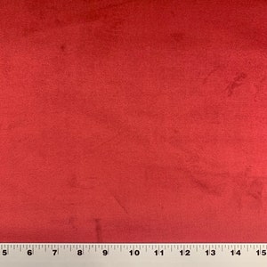 May include: A close-up of a solid red fabric with a slight sheen. The fabric is smooth and has a subtle texture. A ruler is placed at the bottom of the image.
