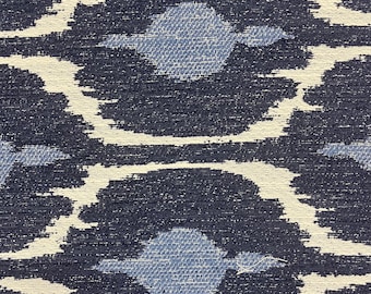 May include: Close-up of a fabric with a repeating pattern. The design features dark navy blue, light blue, and off-white shapes. The shapes resemble stylized floral or geometric motifs, creating a textured, patterned surface.