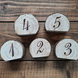 May include: Five wooden slices with numbers 1 through 5 burned into the surface. The slices are arranged in a semi-circle on a wooden surface.