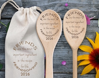 May include: Two light-colored wooden spoons and a beige drawstring fabric bag, each featuring the laser-engraved text: FRIENDS are the most important ingredient in the recipe for life. FRIENDSGIVING 2026.