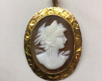 May include: A gold oval cameo pendant with a white cameo of a woman's profile. The pendant has a detailed floral design around the cameo.