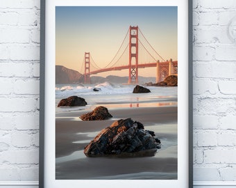 May include: A framed photograph of the Golden Gate Bridge in San Francisco, California. The bridge is red and is seen from a distance, with the water and beach in the foreground.