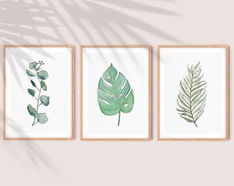 May include: Three framed watercolor prints of green leaves. The first print features a sprig of eucalyptus leaves. The second print features a single monstera leaf. The third print features a single palm frond.