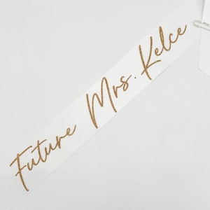 May include: White satin sash with gold glitter lettering that reads "Future Mrs. Kelce".