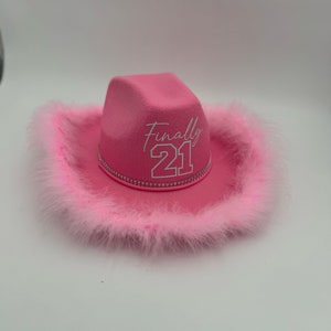 May include: Pink cowboy hat with a white feather trim and the text "Finally 21" embroidered on the front.