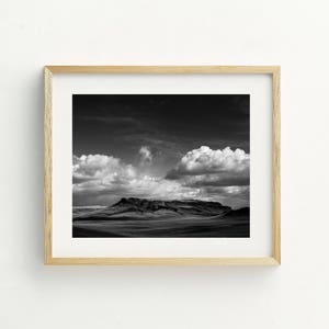 May include: A black and white photograph of a mountain range with dramatic clouds in the sky.
