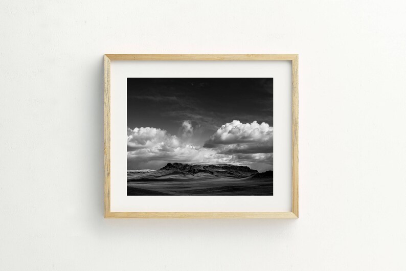May include: A black and white photograph of a mountain range with dramatic clouds in the sky.