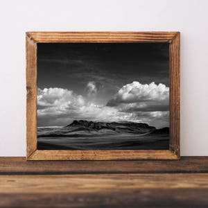 May include: A black and white photograph of a mountain range with a cloudy sky. The photo is framed in a rustic wooden frame.